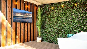 A room with a wooden wall, a large potted plant, a mounted TV, and a green leafy wall.