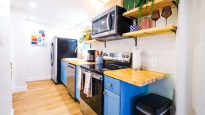 Een kleine keuken met een magnetron, oven en spoelbak, houten aanrechtbladen en blauwe keukenkastjes.