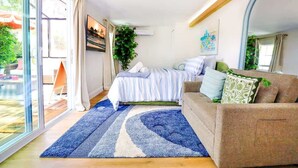 Een slaapkamer met een bed, een slaapbank, een groot raam en een schuifdeur die toegang geeft tot een buitenruimte.