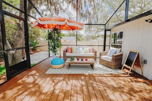 A wooden deck with outdoor furniture, a hanging umbrella, and a chalkboard. - Private UCF Apt | King + Priv Yard + Outdoor Tub (Orlando)