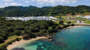 Vista aérea de uma área costeira com vários edifícios brancos, possivelmente um resort ou hotel, rodeados por vegetação densa e um mar azul cristalino.