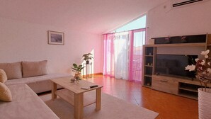 A living room with a sofa, coffee table, TV stand, and a large window with curtains. - Kristalis by Interhome (Medulin)