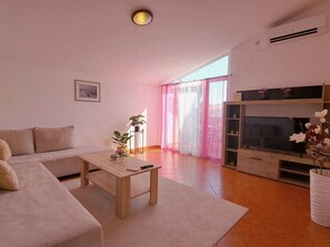 A living room with a sofa, coffee table, TV stand, and a large window with curtains. - Kristalis by Interhome (Medulin)