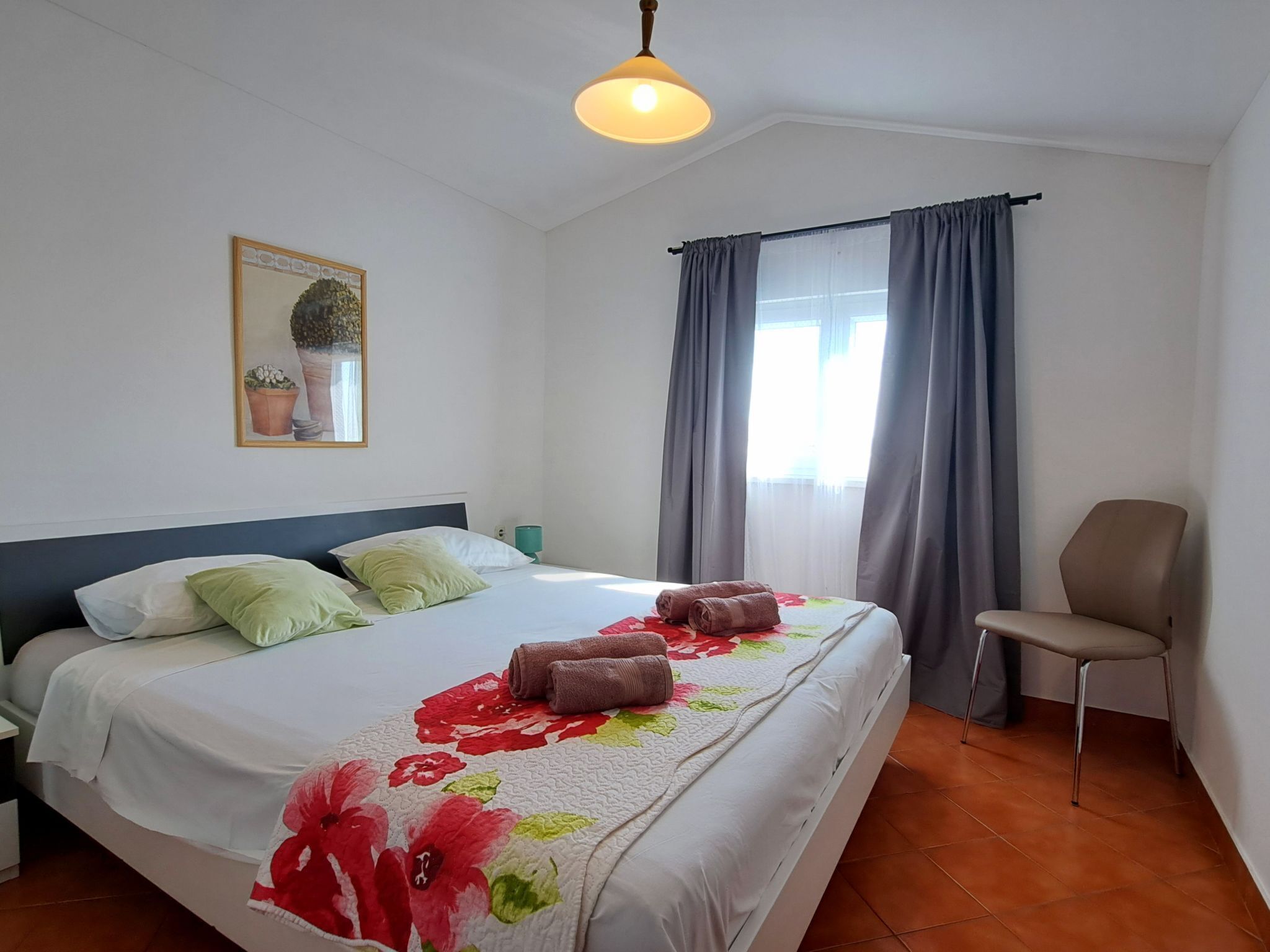 A hotel room with a bed, a chair, a window with curtains, and a ceiling light.