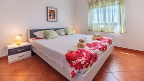 A bedroom with a bed, nightstand, lamp, window with curtains, and a wall-mounted picture. - Kristalis by Interhome (Medulin)