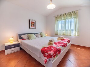 A bedroom with a bed, nightstand, lamp, window with curtains, and a wall-mounted picture. - Kristalis by Interhome (Medulin)