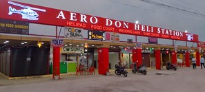 Ein Geschäftsgebäude mit einer roten und weißen Beschilderung mit der Aufschrift 'AERO DON HELI STATION' und verschiedenen Geschäftsschildern, darunter 'Coco Sun' und 'We Crunch'.
