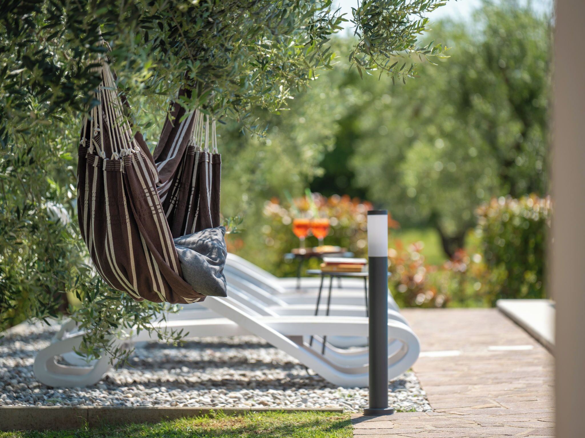 A hammock hanging from a tree, a white lounge chair, and a table with chairs in a garden setting.