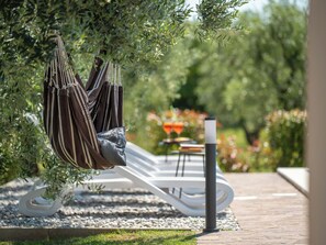 Eine Hängematte, die an einem Baum befestigt ist, ein weißer Liegestuhl und ein Tisch mit Stühlen in einem Garten.