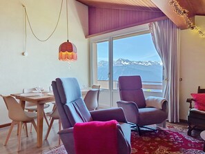 Ein Zimmer mit Esstisch, Stühlen, Bergblick und einem Balkon mit Vorhängen.