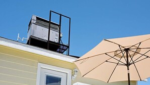 Une terrasse en bois peinte en blanc, avec une porte blanche, un parasol beige et une balustrade blanche.