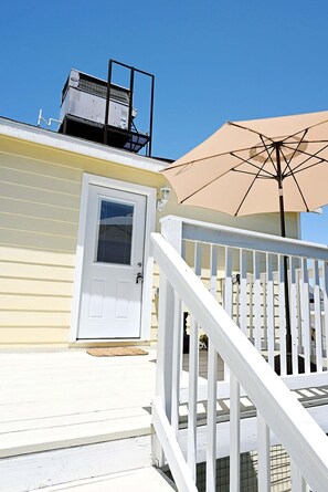 Une terrasse en bois peinte en blanc, avec une porte blanche, un parasol beige et une balustrade blanche.