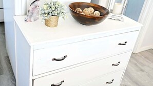 Une commode blanche avec des tiroirs, un bol contenant des objets décoratifs, une petite plante et une lanterne.