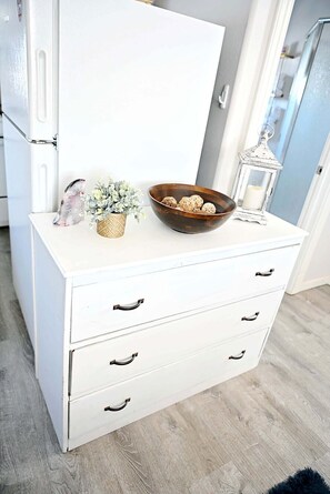 Une commode blanche avec des tiroirs, un bol contenant des objets décoratifs, une petite plante et une lanterne.