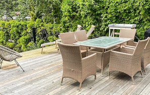 Een tuinmeubelset van riet met een glazen tafel en stoelen, staand op een houten terras.