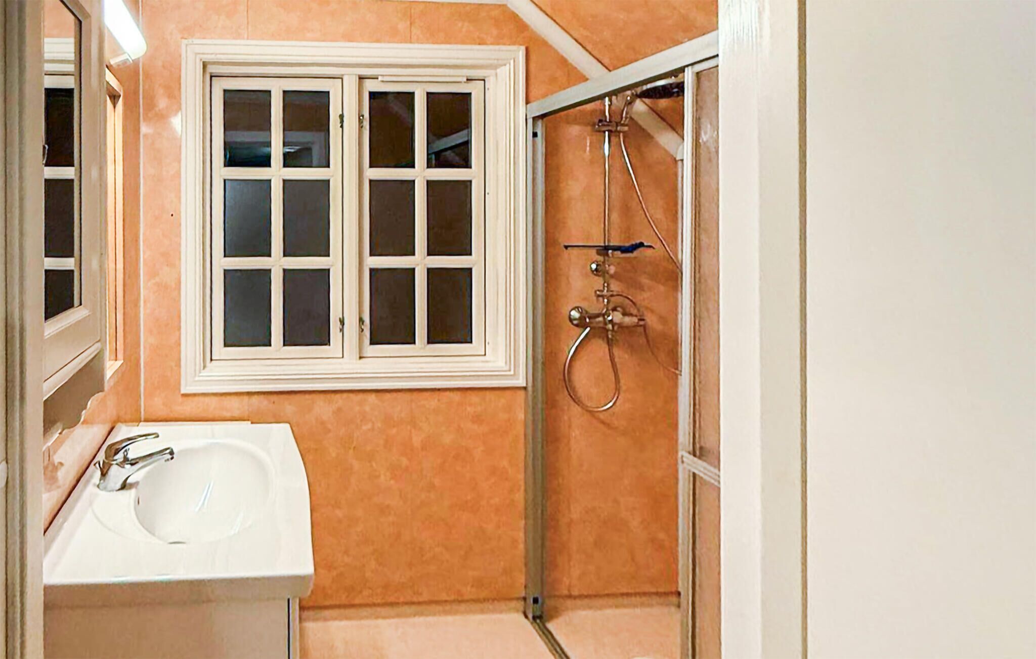 Une salle de bain avec un lavabo blanc, une fenêtre à cadre blanc et un espace douche doté d’une porte en verre.