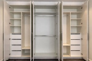 A walk-in closet with multiple shelves and drawers, a central door, and a mirrored closet door. - Modern 2BR 3 min to Central Station FREE Parking (Chippendale)