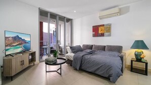 A modern living room with a bed, a TV, a small table, and a balcony with a view. - Modern 2BR 3 min to Central Station FREE Parking (Chippendale)