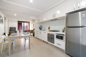 A modern kitchen with white cabinetry, a stainless steel refrigerator, a built-in oven, and a dining area with a table and chairs. - Modern 2BR 3 min to Central Station FREE Parking (Chippendale)