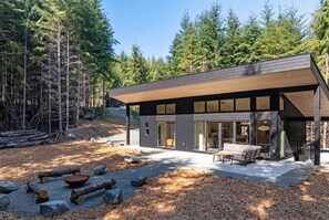 Ein modernes Haus mit überdachter Terrasse, großen Fenstern und Wald im Hintergrund.