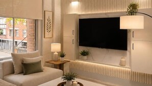 Ein modernes Wohnzimmer mit einem Ecksofa, einem Flachbildfernseher an der Wand und einem Beistelltisch mit Lampe und Dekoration.