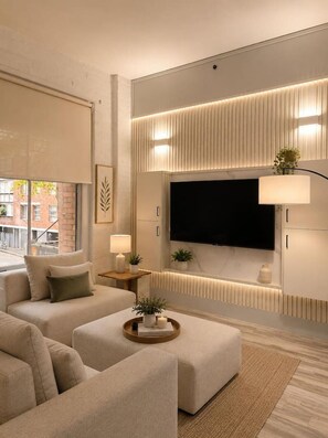 A modern living room with a sectional sofa, a flat-screen TV mounted on the wall, and a side table with a lamp and decorative items. - Classic City Unit with Parking and walk to Harbour (Pyrmont)