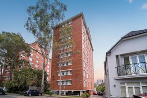 A multi-story residential building with a brick facade, multiple balconies, and a parking area in front. - Cozy 1 Bed Harbour View Apartment and Free Carpark (North Sydney)