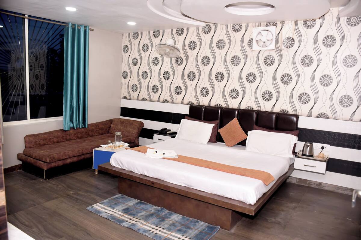 Ein modernes Hotelzimmer mit einem großen Bett, einer Couch, einem Nachttisch und einem Fenster mit Vorhängen.