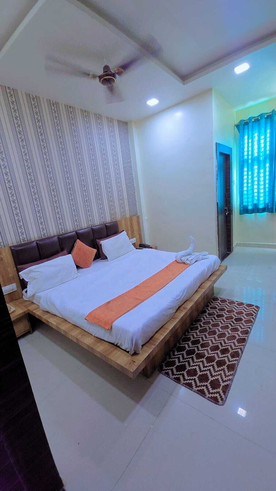 A hotel room with a bed, a ceiling fan, a patterned wall, and a window with curtains.