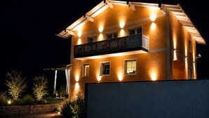 Un edificio a due piani con un balcone, finestre illuminate e un ingresso ben illuminato.
