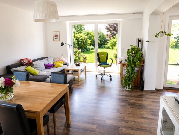 Un salon moderne avec un canapé, une table à manger et une grande fenêtre donnant sur un jardin.