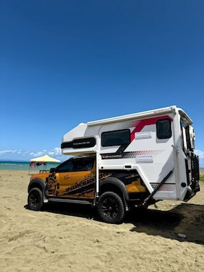 Un camper bianco e giallo parcheggiato su una spiaggia sabbiosa sotto un cielo azzurro limpido.