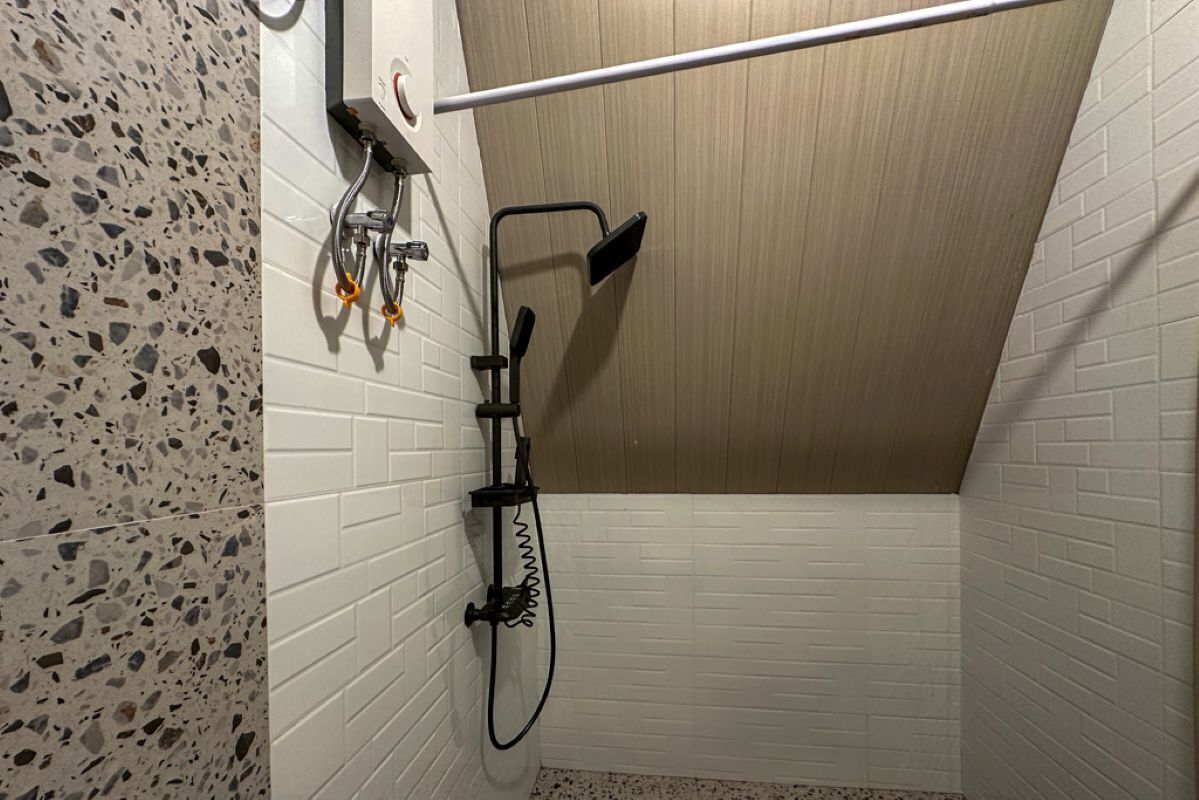 Una ducha con cabezal de ducha de mano, panel de control en la pared y un perchero.