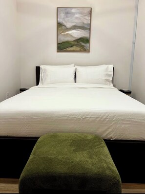 A bedroom with a bed, a green ottoman, a nightstand, and a painting on the wall. - Brick & Bed - Arch, Casino, Convention Center, T-410 (St. Louis)