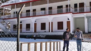 A building with a covered balcony, a staircase, and a fenced area with snow. - Swastik Hotel and Restaurant (Banglo Ki Kandi)