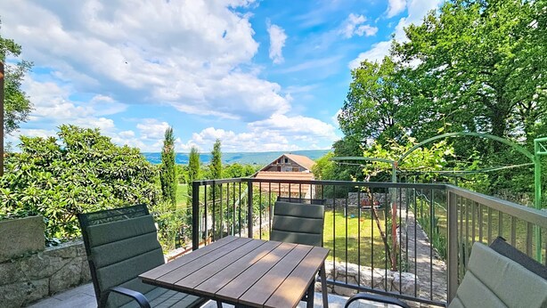 An outdoor patio with a table and chairs, surrounded by a metal railing and greenery. - Vacation home Orba by Interhome (Imotski)