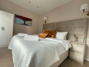 Ein ordentlich bezogenes Bett mit einer gesteppten Decke, ein Nachttisch mit einer Vase und ein Gemälde an der Wand.