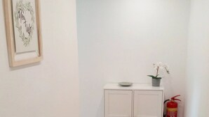 Un couloir avec un tapis à motifs, une armoire blanche, une œuvre d’art encadrée et un extincteur.