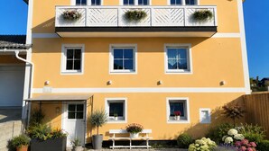 Un immeuble à plusieurs étages doté de balcons, d’une entrée principale et d’un jardin agrémenté de plantes et de fleurs en pot.