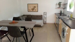 Un espacio habitable compacto con sofá, mesa de comedor, sillas, lavadora y zona de cocina.