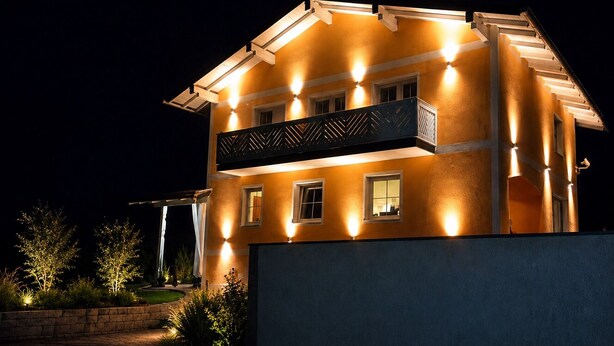 Un immeuble de deux étages doté d’un balcon, de fenêtres illuminées et d’une entrée bien éclairée.