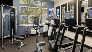 Et fitnessrum med træningsudstyr, store vinduer og en loftsvifte.