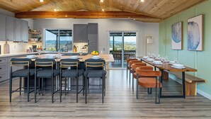 A spacious kitchen with a large island, modern bar stools, and a dining area with a long table set for a meal. - Rainer Estate (Seattle)