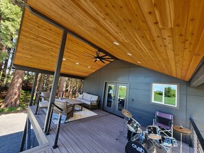A covered deck with a ceiling fan, a drum set, and a seating area with a table and chairs.