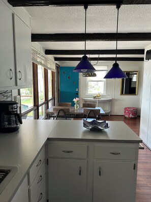 A kitchen with a coffee maker, a dining area with a table and chairs, and a blue door.