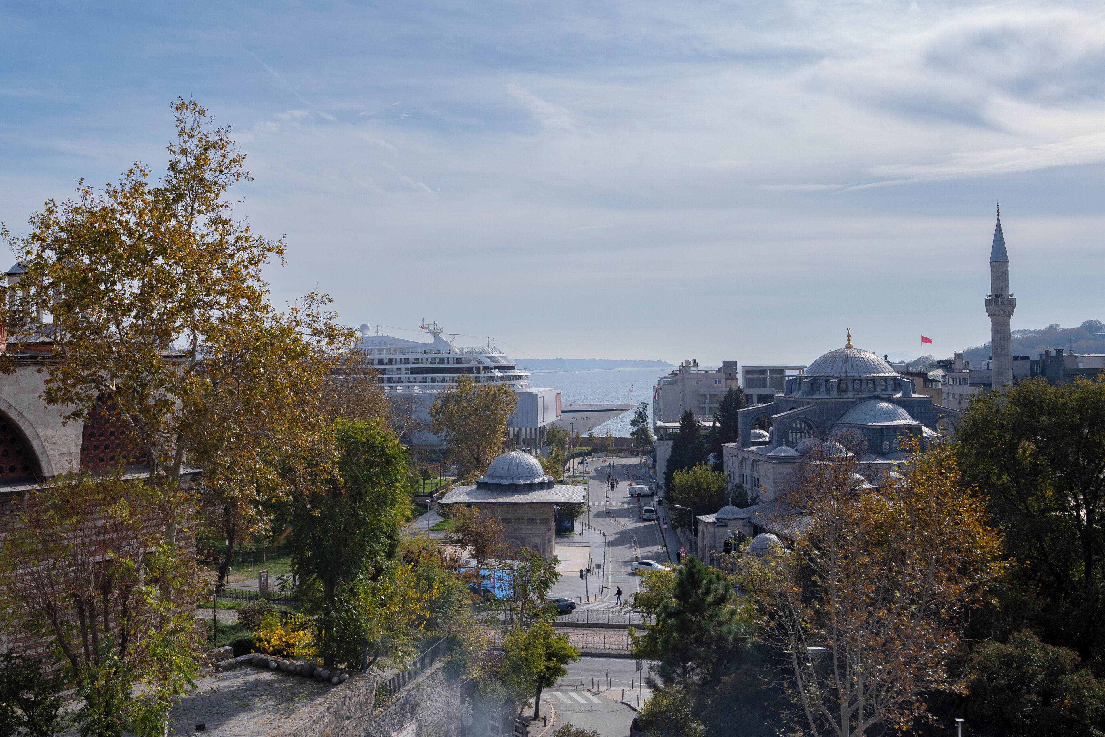 Stadtansicht mit historischen Gebäuden, einer Moschee mit Minarett und Blick auf das Meer.