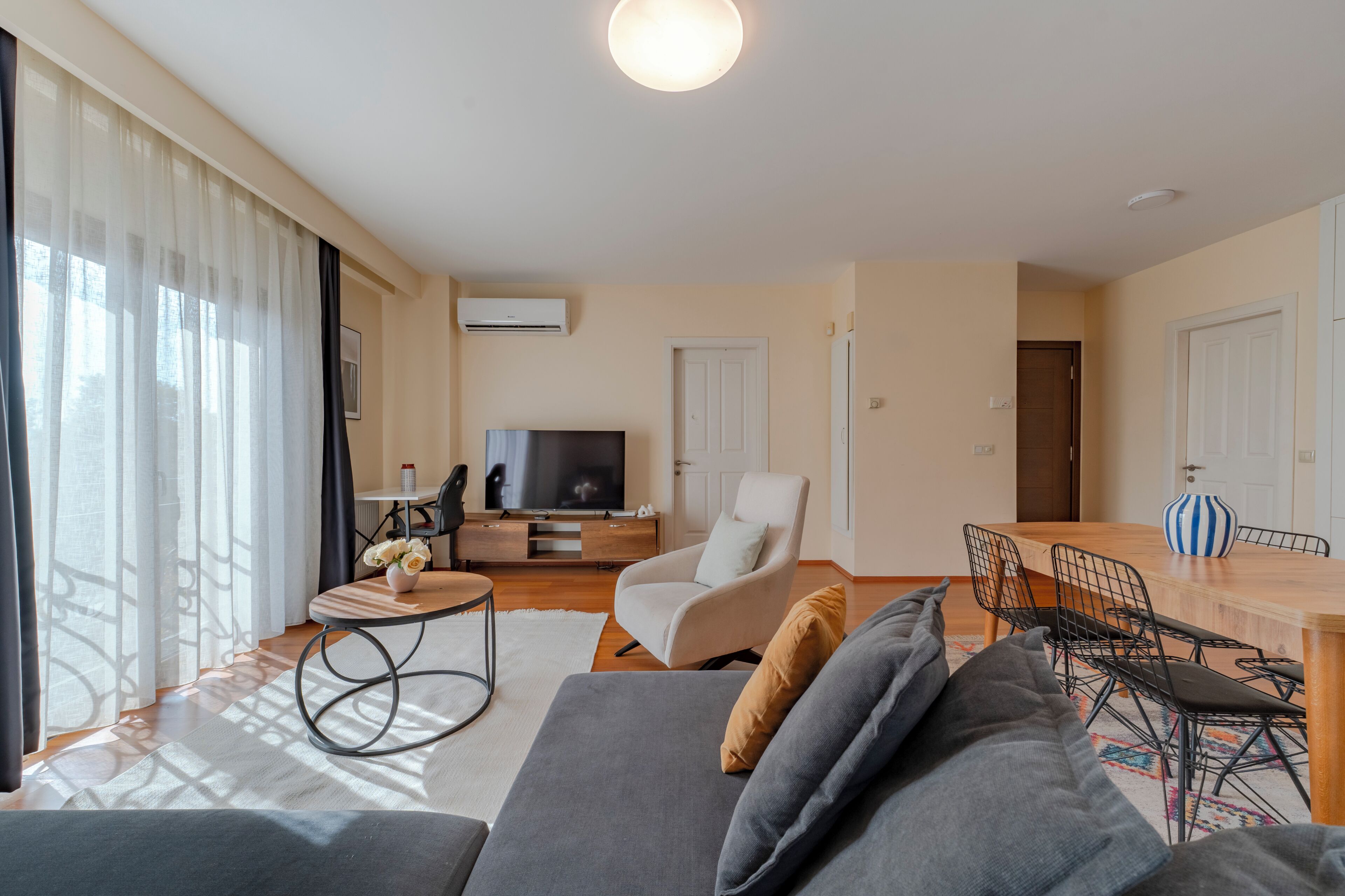 A modern living room with a sofa, TV, dining area, and large windows.