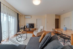 A modern living room with a sofa, TV, dining area, and large windows. - Spacious One-Bedroom Apartment with Bosphorus View (İstanbul)