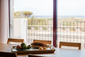 Ein Esstisch mit Obstschale und einer Papaya auf einer Holzwage, mit Blick auf einen Balkon und eine Meerlandschaft.