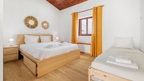 A bedroom with a wooden bed, a smaller bed, a nightstand with a lamp, and a window with curtains. - Casa Forno de Cal - By WeHostMadeira (Porto Santo)